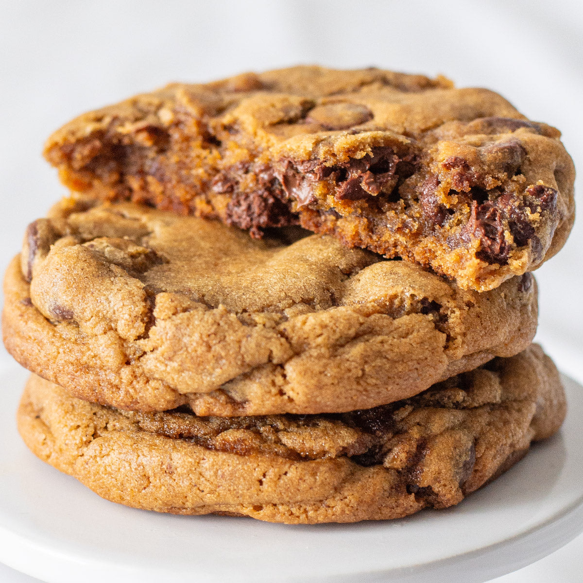 A stack of three Harvest Spice Chocolate Chip Cookies, with the top cookie broken in half to reveal its soft, gooey interior.