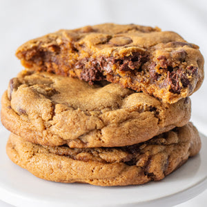 A stack of three Harvest Spice Chocolate Chip Cookies, with the top cookie broken in half to reveal its soft, gooey interior.