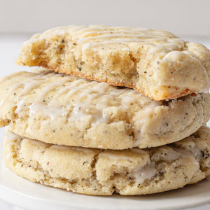 A stack of London Fog Latte Cookies, with one cookie broken in half to reveal flecks of earl grey tea infused into the cookie dough, topped with a vanilla bean glaze.