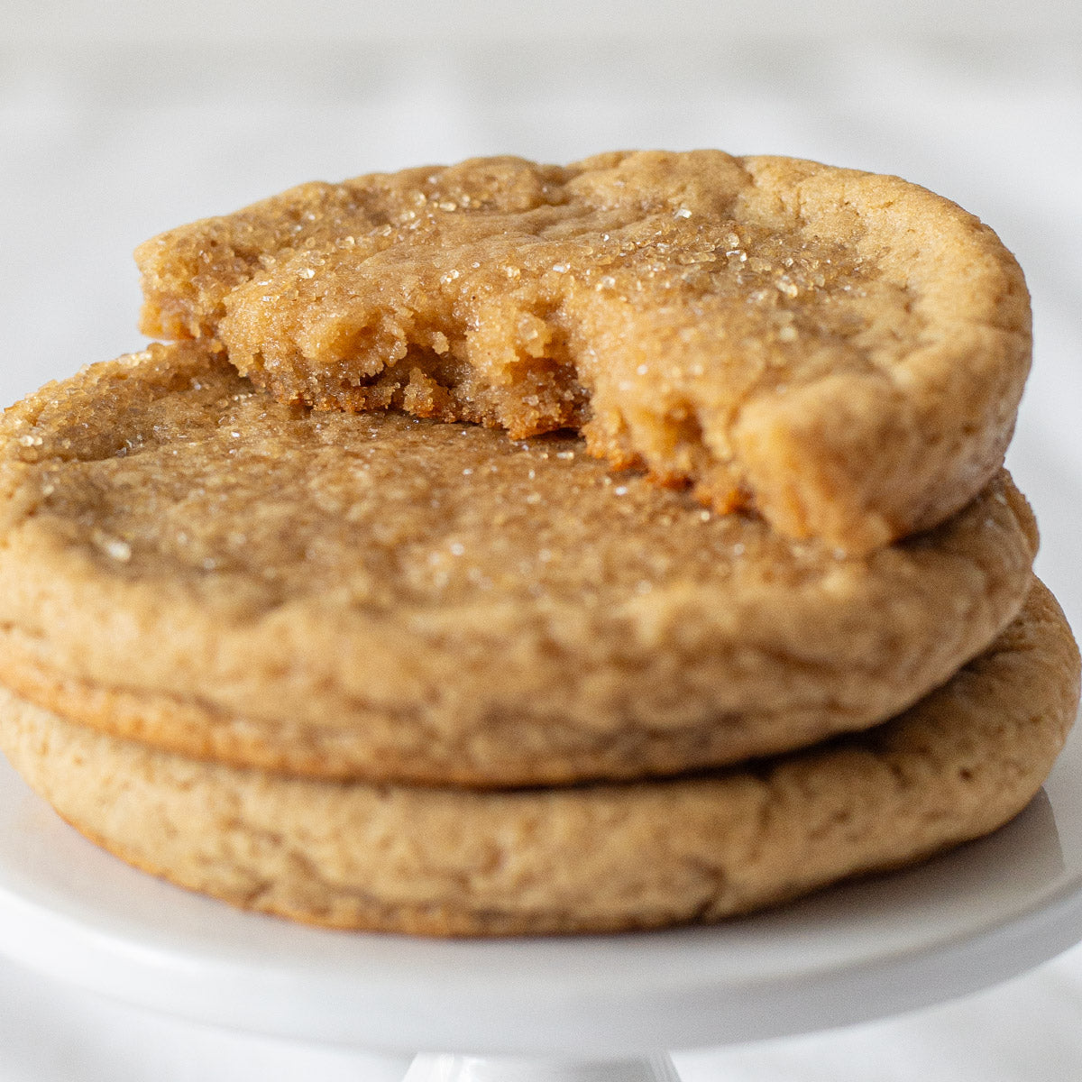 Three stacked Maple Sugar Cookies, with the top cookie broken in half to reveal a soft, tender interior, highlighting the golden-brown texture and sugar crystals on the surface.