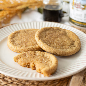 A plate of Maple Sugar Cookies with a small jar of maple syrup in the background, emphasizing the rich maple flavor of the cookies.