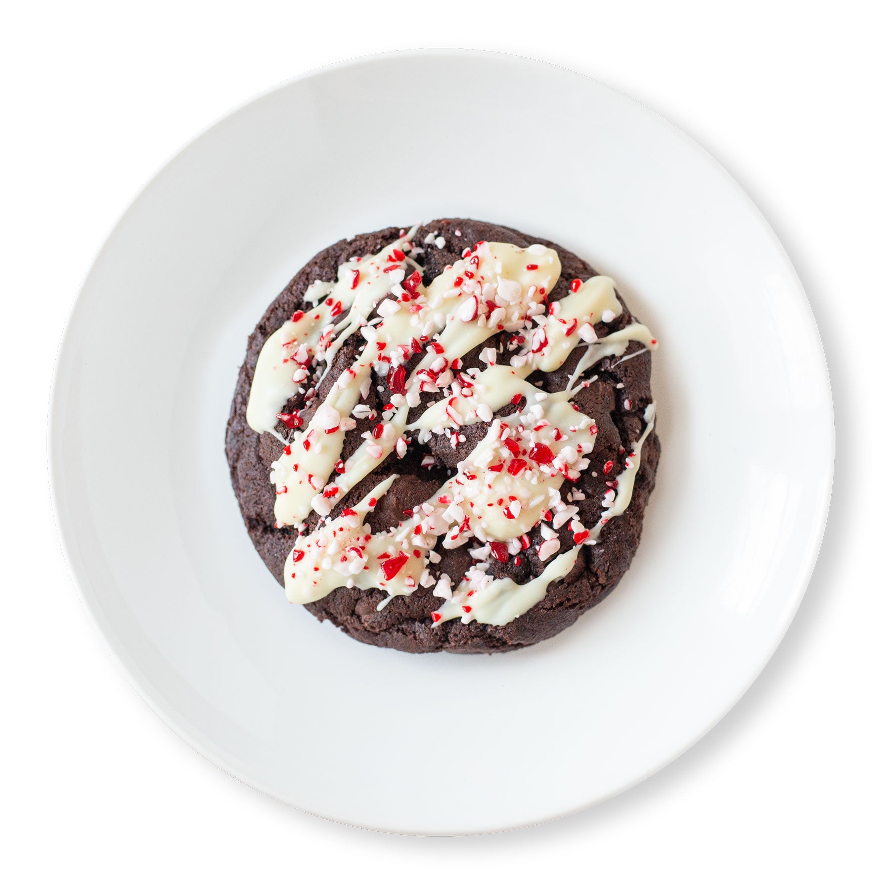 A single chocolate peppermint mocha cookie on a white plate. The cookie is drizzled with white chocolate and topped with crushed peppermint candy pieces, creating a festive, holiday-inspired treat.