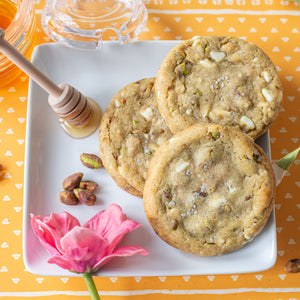 Close-up of Salted Honey Pistachio Cookies, showcasing their golden-brown color, speckled with chunks of pistachios and white chocolate chips, and topped with a sprinkling of sea salt flakes.